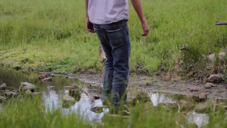 El-Joven-Cruza-Frente-A-La-Cámara,-Atraviesa-El-Arroyo-Y-Se-Aleja-Caminando-Hacia-El-Campo