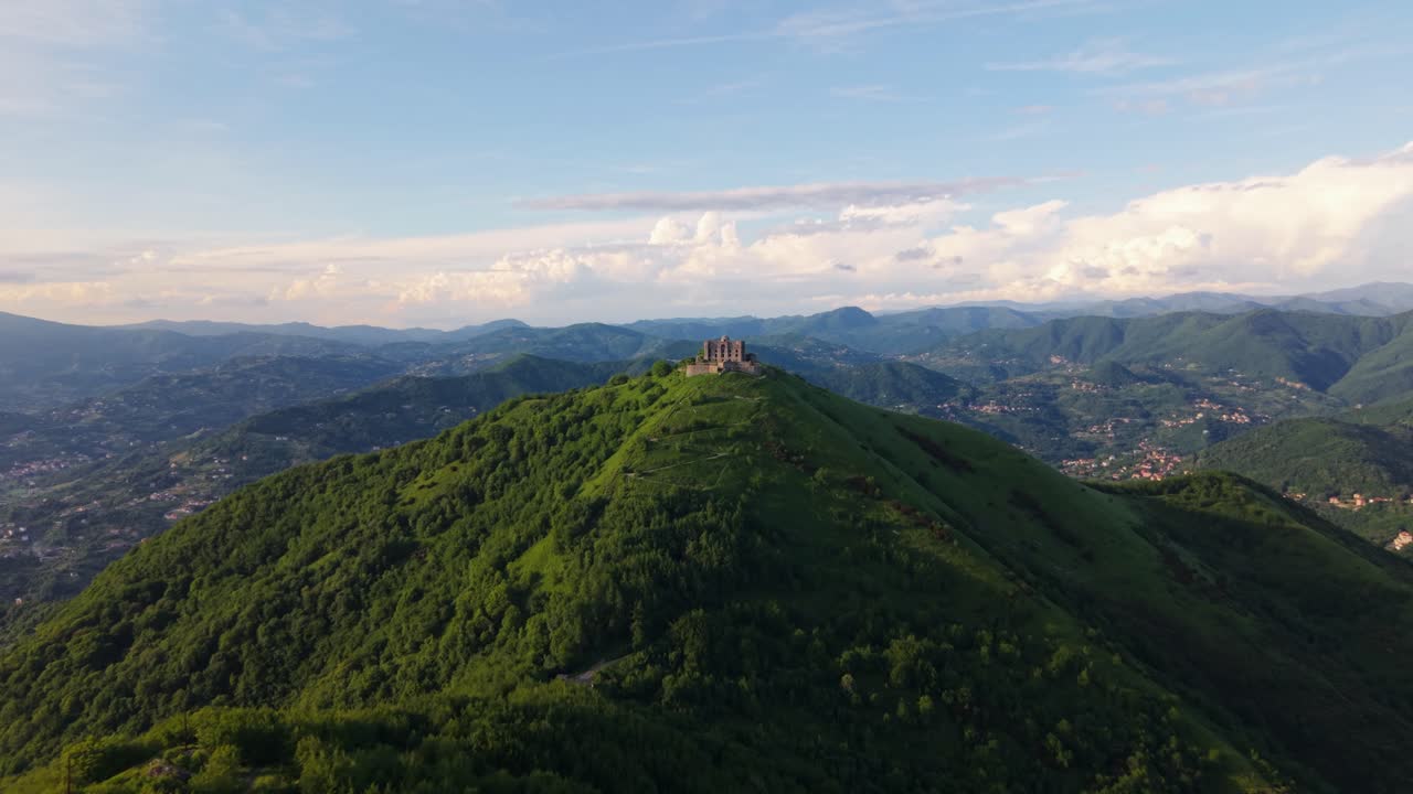 Ancient fort on a hill in Italy surrounded by lush greenery and mountains