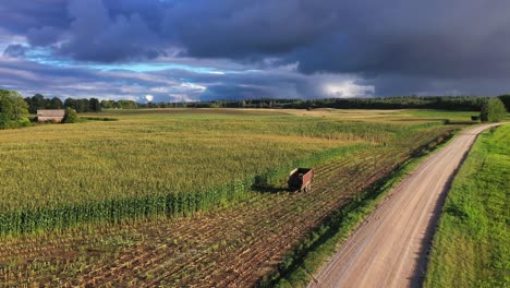 empty tractor trailer on partly harvested cornfield in golden hour with storm clouds