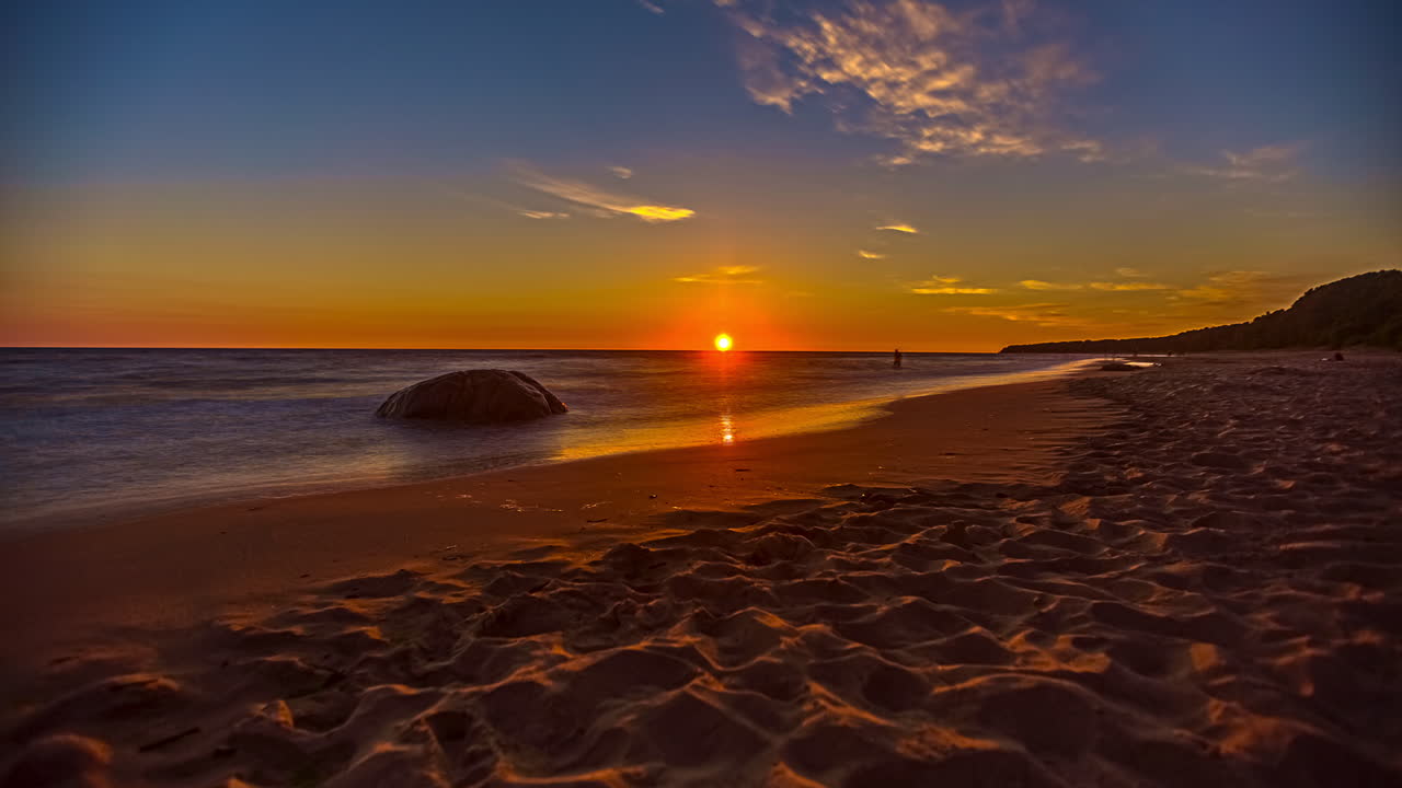 Wavy sand and sea sunset with blue and yellow colors and a sunburst