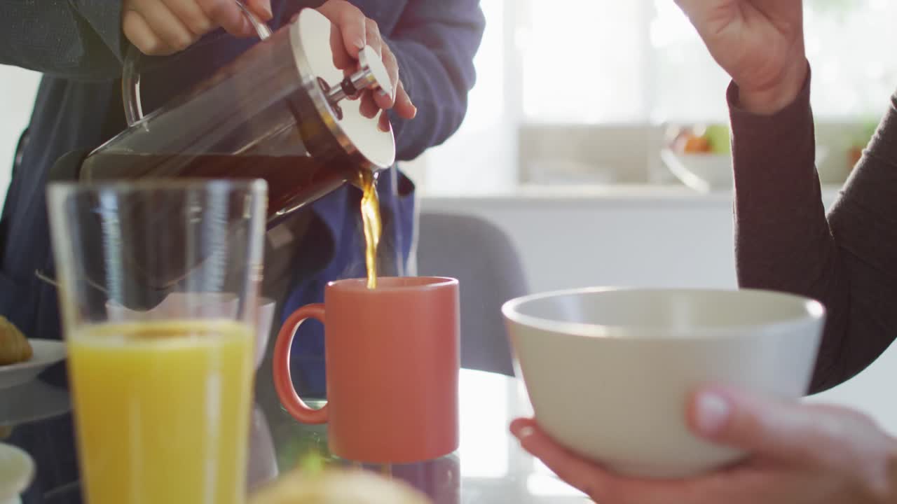 Una donna caucasica a mezzo busto che versa il caffè in una tazza a casa