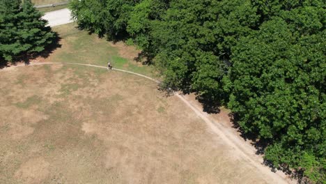 A-aerial-view-following-a-man-jogging-in-a-dry-park-on-a-sunny-day