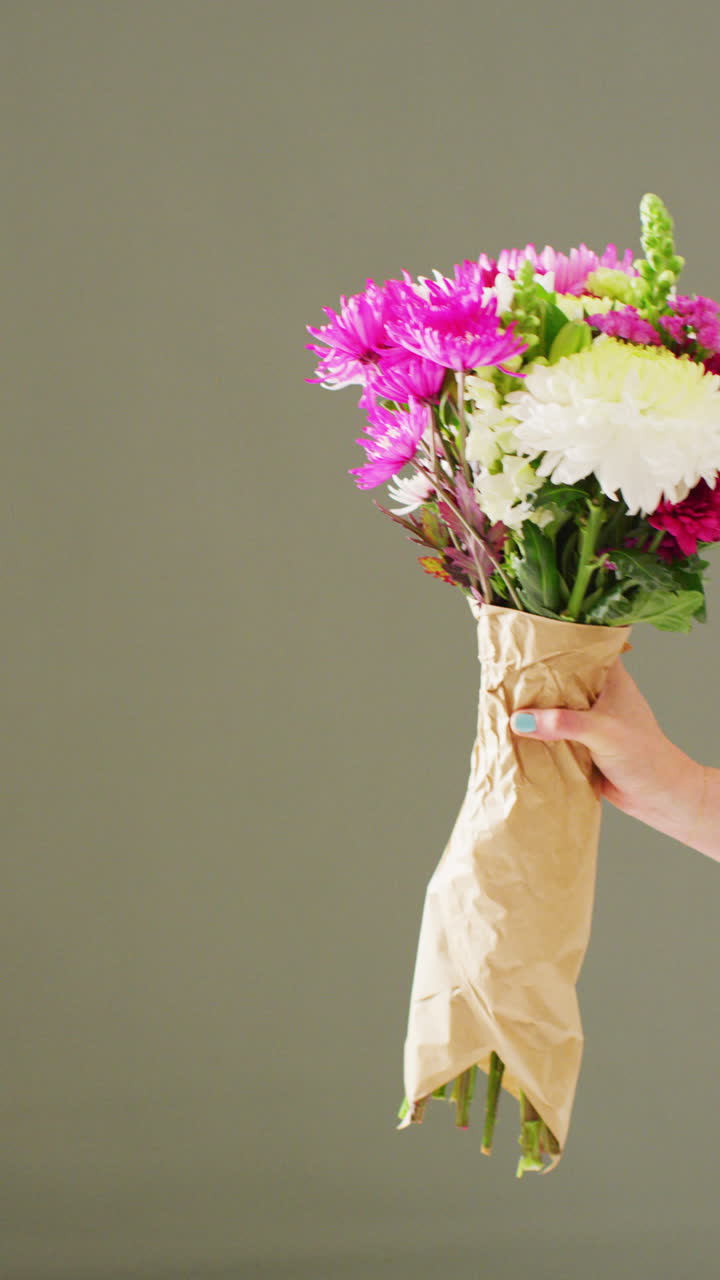 Vertical video of woman holding bunch of flowers with copy space on grey background