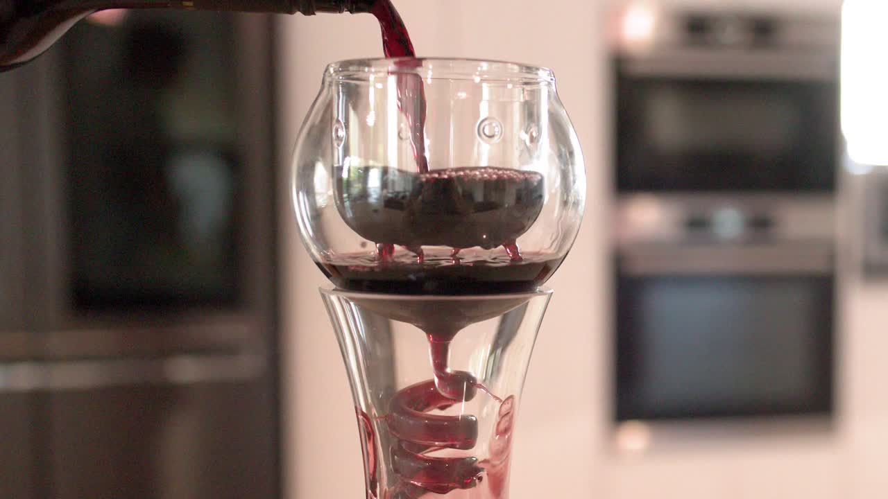 Vino tinto fluyendo a través de un decantador aireador de cristal en espiral en una cocina moderna y luminosa