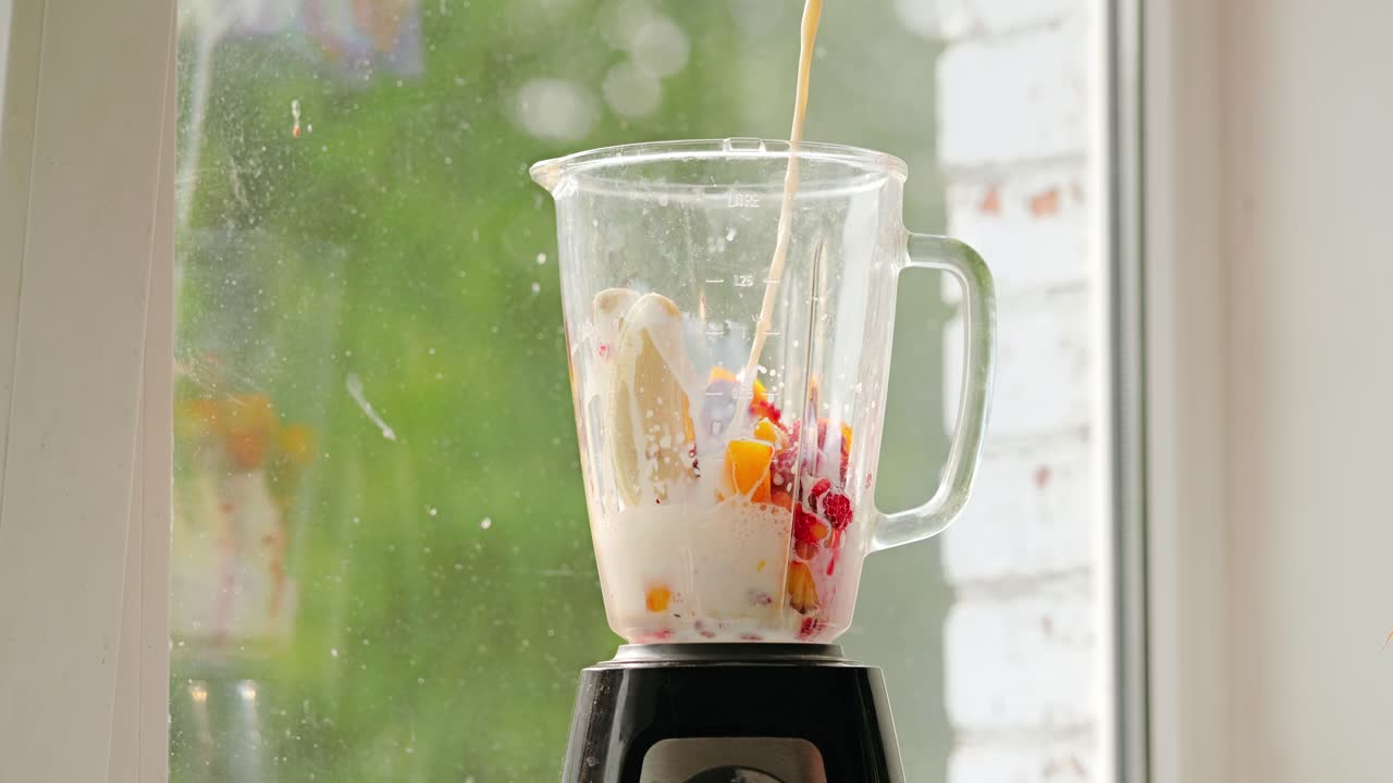 Banana, mango and raspberry mix with milk for creamy smoothie in kitchen light