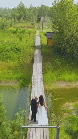 happy just married couple walks on old wooden bridge over narrow river in park backside aerial view