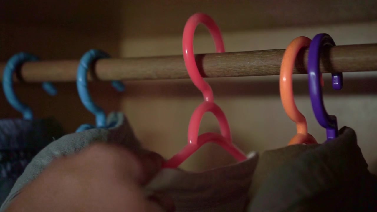 hand of people hanging clothes back on colorful hangers in closet. Wardrobe, fashion, and home organization concept indoor lifestyle footage.