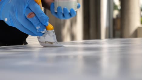close-up of hands in blue gloves painting a surface with a brush