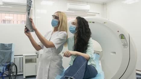 la radióloga explica los resultados de la tomografía computarizada para una paciente joven, mostrando la instantánea con imágenes, observando y analizando la tomografía computada en una clínica moderna junto a un escáner computarizado moderno
