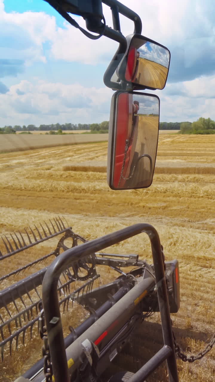 Close-up combine working in summer. Detail of grain harvester collecting ripe wheat on the field. Part of agricultural machine in a bright day. Vertical video