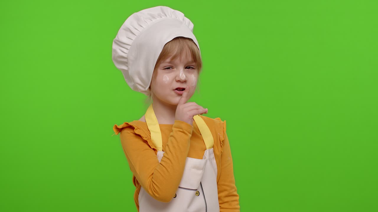 Bambina vestita da cuoca con il dito sulle labbra su sfondo chroma key, gesto di silenzio, segreto.