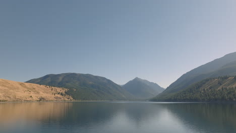 Vista-Aérea-Que-Se-Inclina-Hacia-El-Lago-Alpino-Con-Montañas-En-El-Fondo