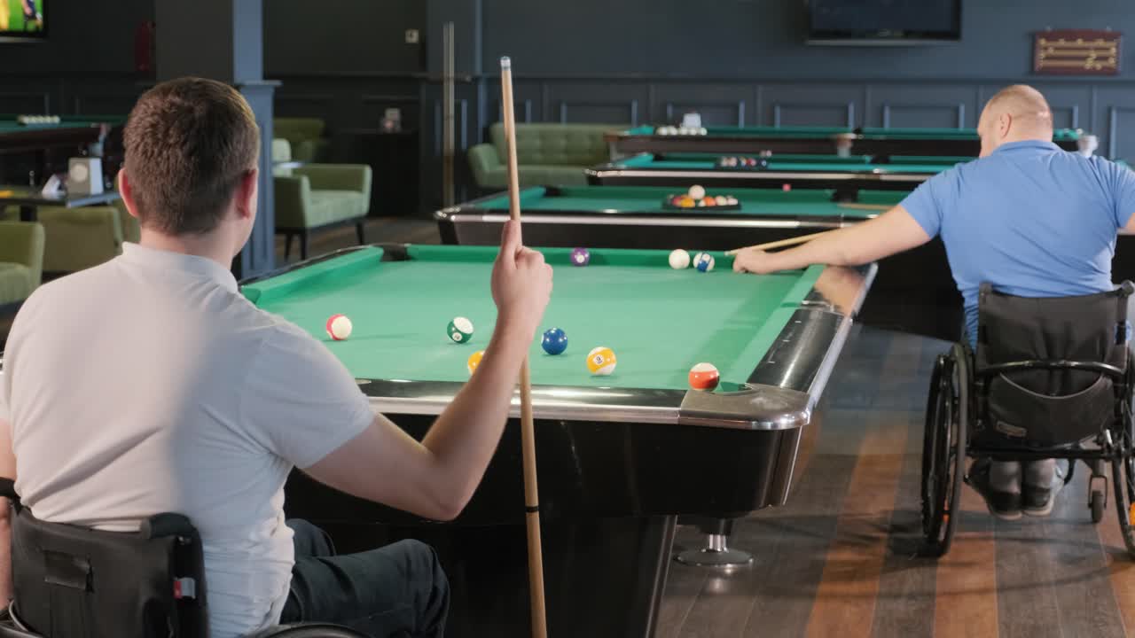 Adult men with disabilities in a wheelchair play billiards in the club
