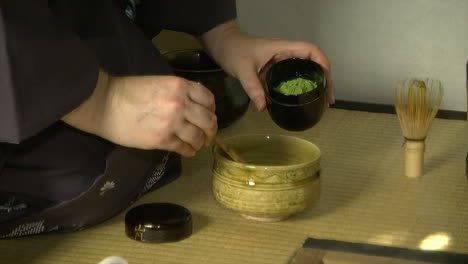 powdered matcha green tea is scooped into a tea bowl during a japanese tea ceremony