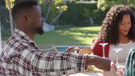 happy diverse male and female friends saying prayer on thanksgiving celebration meal in sunny garden