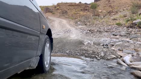 sedan car driving in rural road in nature dust road close near to the rice paddy palm garden farmland fields in baluchistan iran in hot summer day cross the little pond stream side shot the moving car