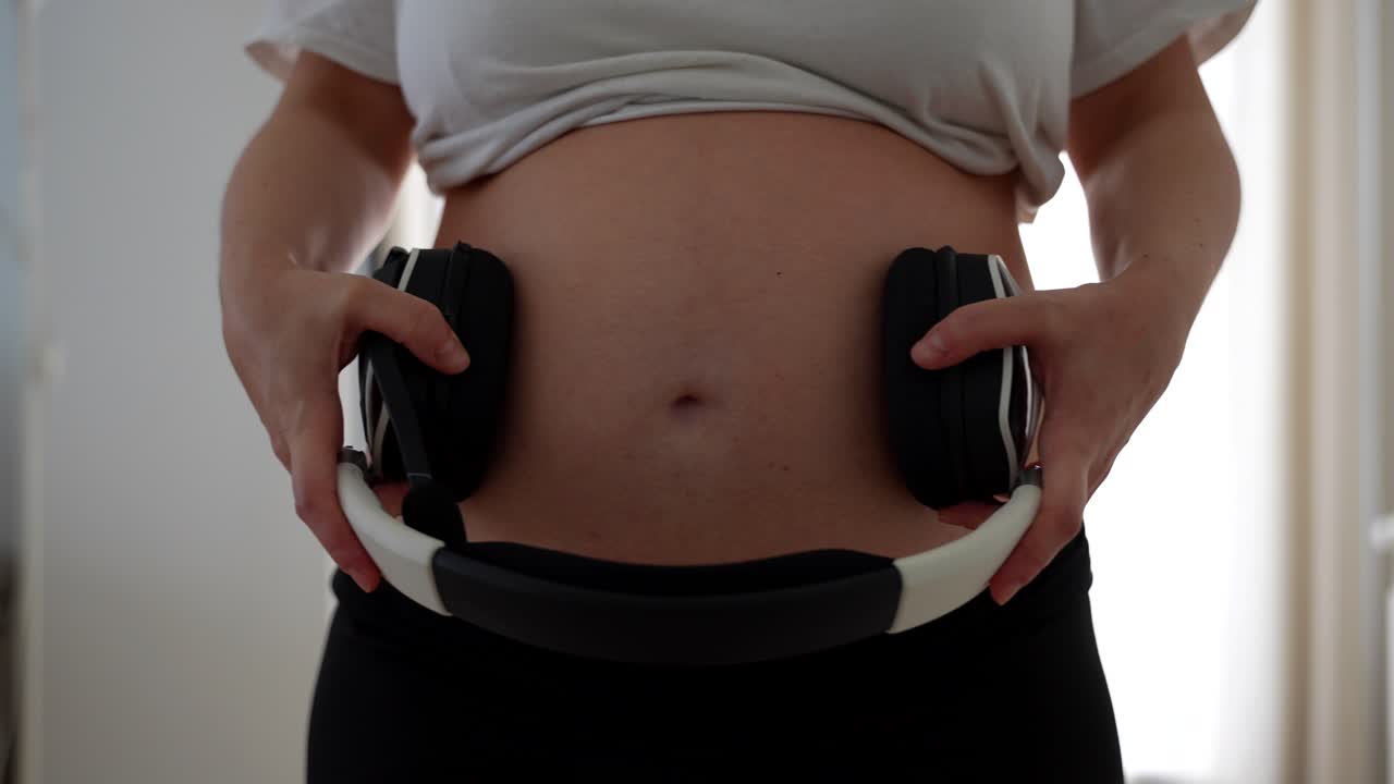 Donna incinta posiziona le cuffie sulla pancia per far ascoltare musica al nascituro.