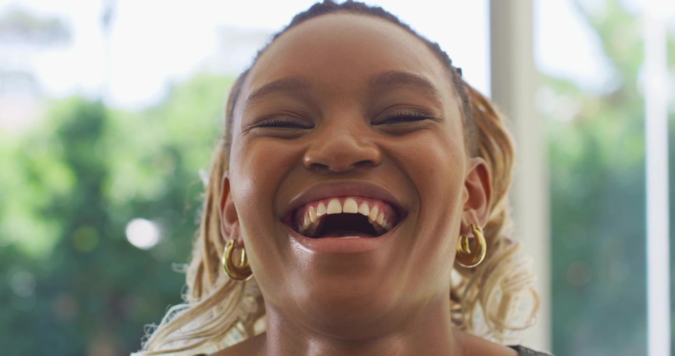Donna afroamericana che sorride, trasformando il sorriso in una risata in risposta a un segnale in studio, con orecchini a cerchio d'oro
