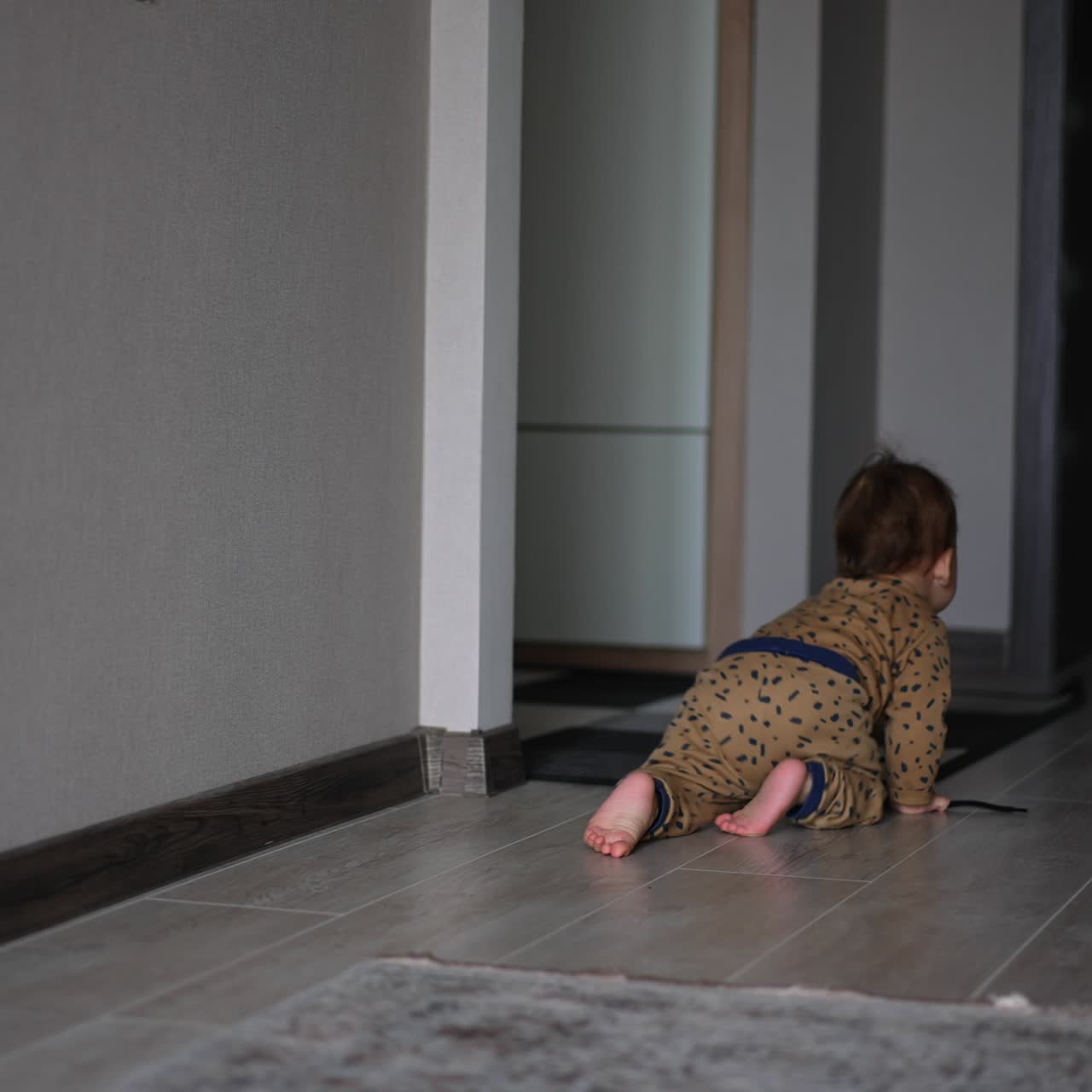 Little baby crawling by the floor towards the door in the room. Lovely kid holding a black cord in his hands