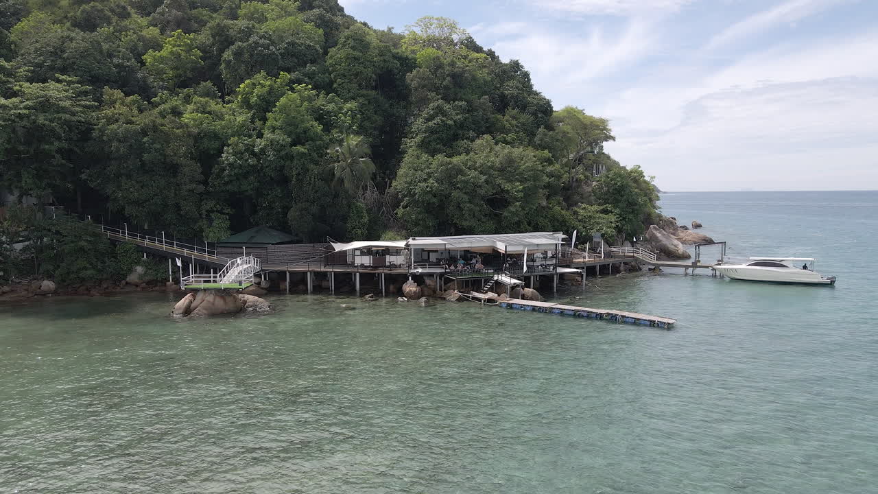 Aerial flight slowly moving towards a remote island dock and building at a jungle resort. Filmed at the Alunan Resort in Penang Kecil Malaysia.