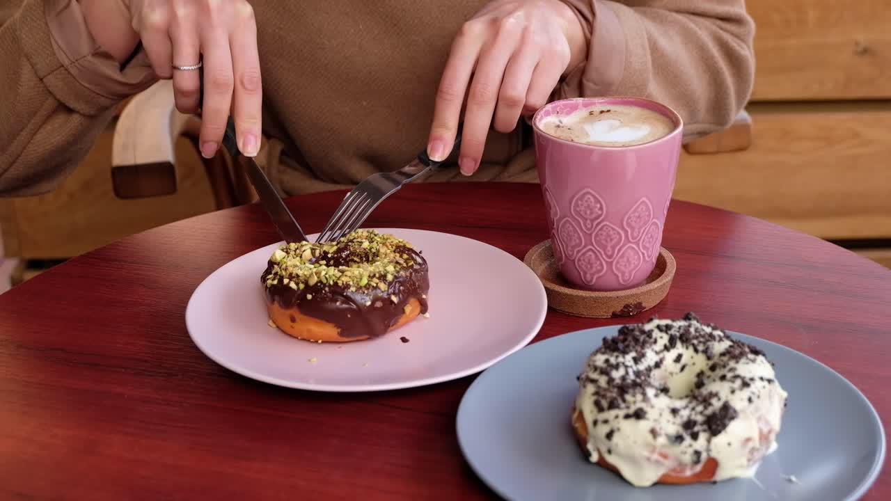 Close up of a woman in a brown coat eating donuts and drinking coffee at a cafe