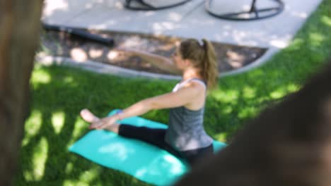 Toma-En-Cámara-Lenta-Panorámica-Desde-Detrás-De-Un-árbol-Y-Revelando-A-Una-Mujer-Haciendo-Yoga-En-Una-Alfombra-De-Yoga