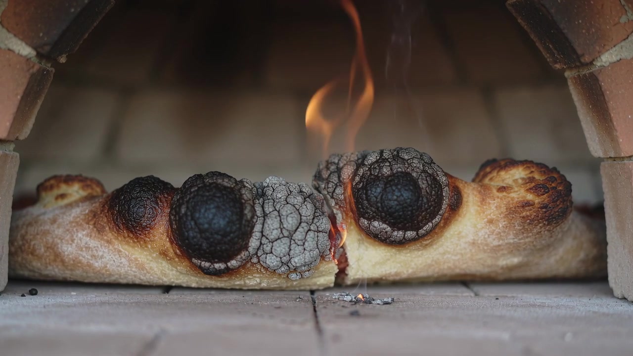 Baking flatbread blistering and cracking inside wood-fired brick oven, embers fueling seam flame