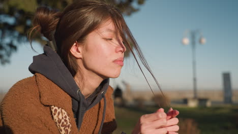 a close-up shot of a girl wearing a brown coat, looking deeply sorrowful and anxious as she pulls at a strand of her hair. her expression conveys a sense of distress and contemplation