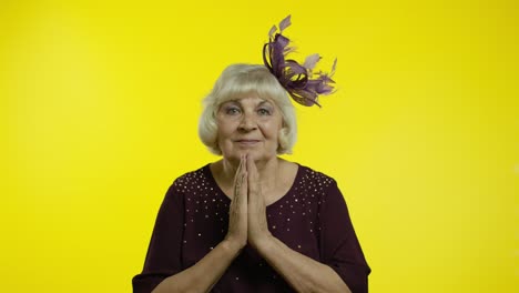 positive senior old blond woman appealing to camera, keeping prayer gesture and asking help