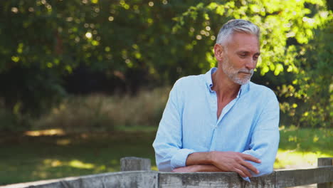 portrait of casually dressed mature man leaning on fence on walk in countryside