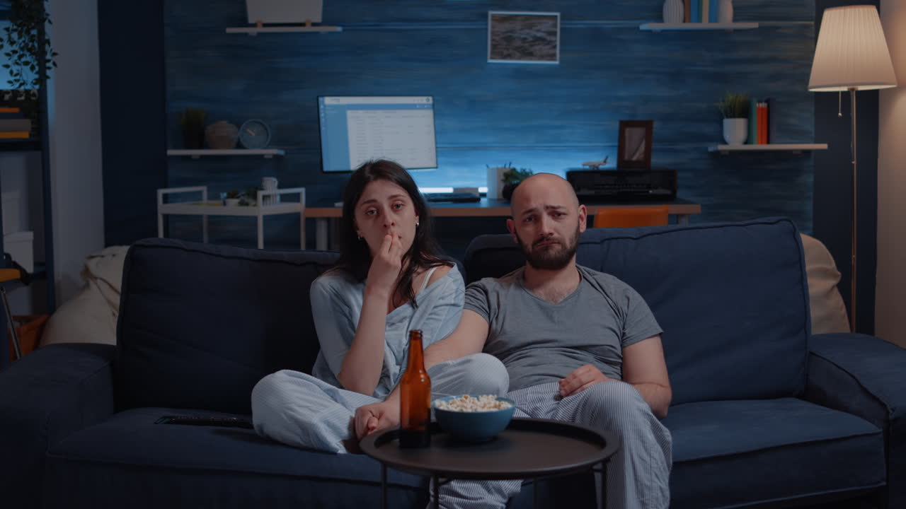 Coppia sensibile che guarda un film drammatico in TV, piangendo seduta sul divano