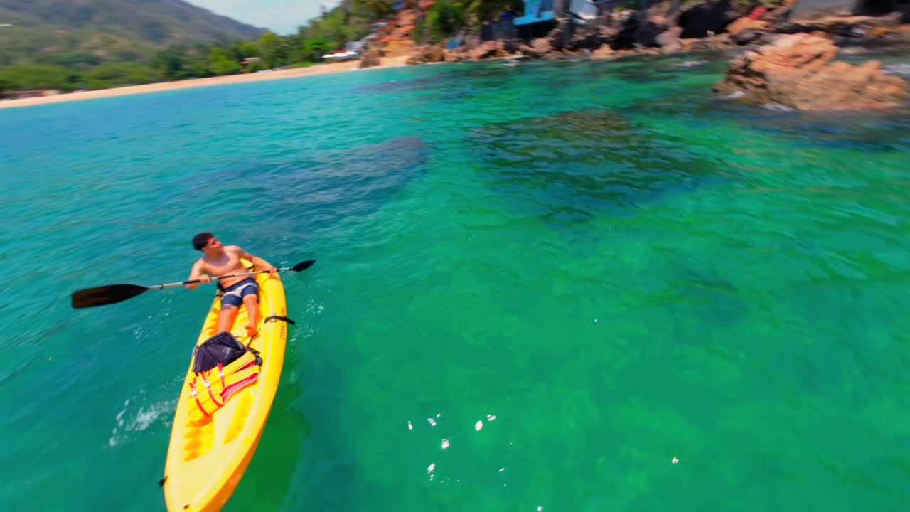 FPV drone orbits young man kayaking in clear turquoise waters at Yelapa ...
