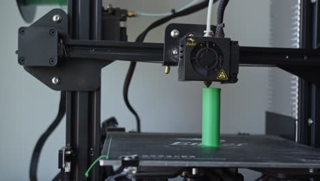 black 3d printer printing a small green plastic element