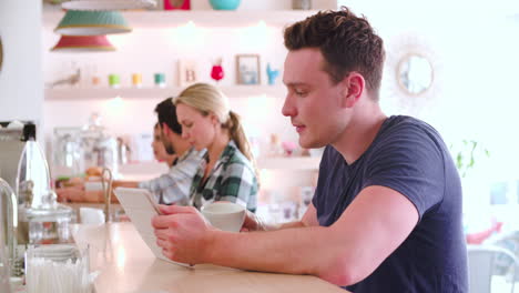 Un-Joven-Usando-Una-Tableta-Sentado-En-Una-Cafetería