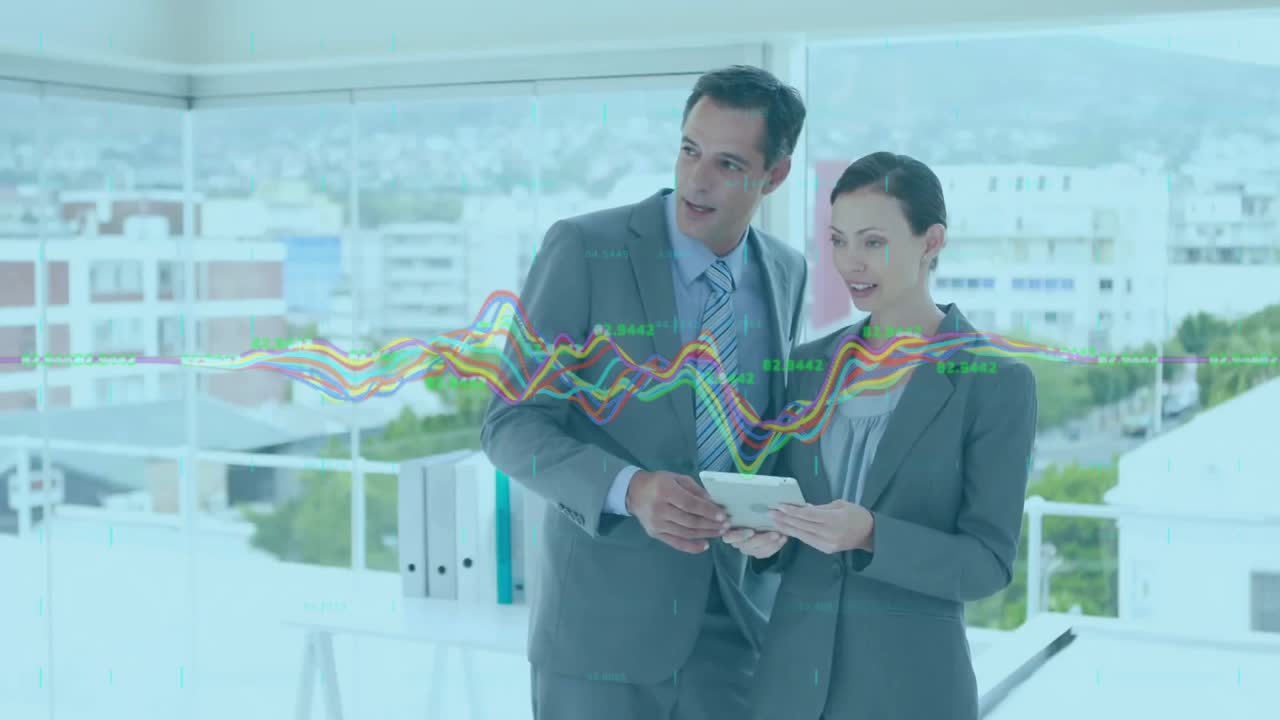 Mulher tocando no tablet, animando gráficos de dados enquanto colega analisa números em escritório corporativo.