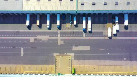 Aerial-view-of-a-semi-trucks-with-cargo-trailers-standing-on-warehouses-ramps-for-loading-unloading-goods-on-the-big-logistics-park-with-loading-hub