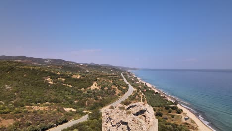 Aerial-drone-clip-ascending-over-an-ancient-ruined-tower-and-a-beach-in-Kavala,-Macedonia,-Greece