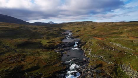 glacial river stream flowing through steep norwegian highlands with waterfalls and mountains. aerial drone.