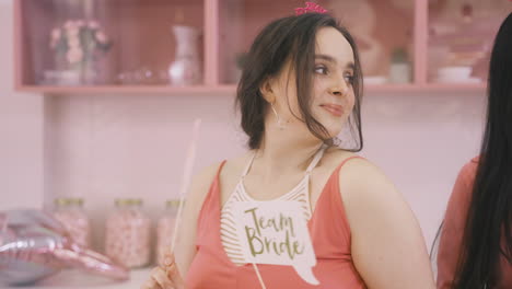 Close-Up-View-Of-Brunette-Woman-With-Headdresses-And-Holding-Cardboard-Decoration-Dancing-In-A-Pink-Room-Celebrating-A-Bachelorette-Party