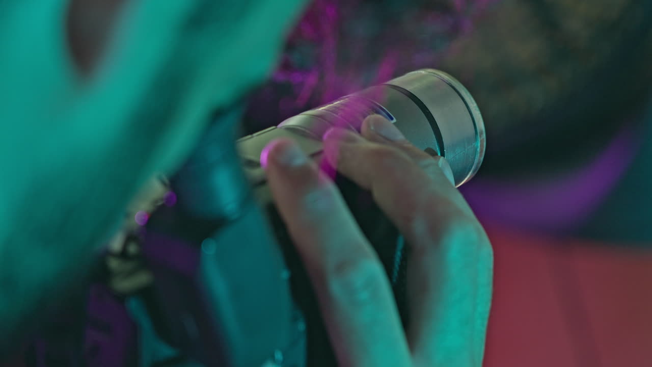 Primo piano di mani che azionano una videocamera vintage sotto luci al neon