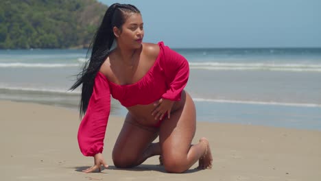 On-the-beach,-a-girl-in-a-striking-red-bikini-lies-gracefully-on-the-soft-sand,-while-the-gentle-ebb-and-flow-of-the-ocean-waves-form-a-captivating-backdrop