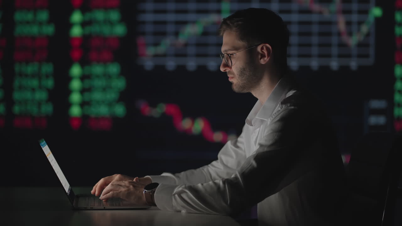 Young Caucasian man trader working at monitor laptop and browsing online in trading office. Male broker following rates and bets. Manager texting at screen.