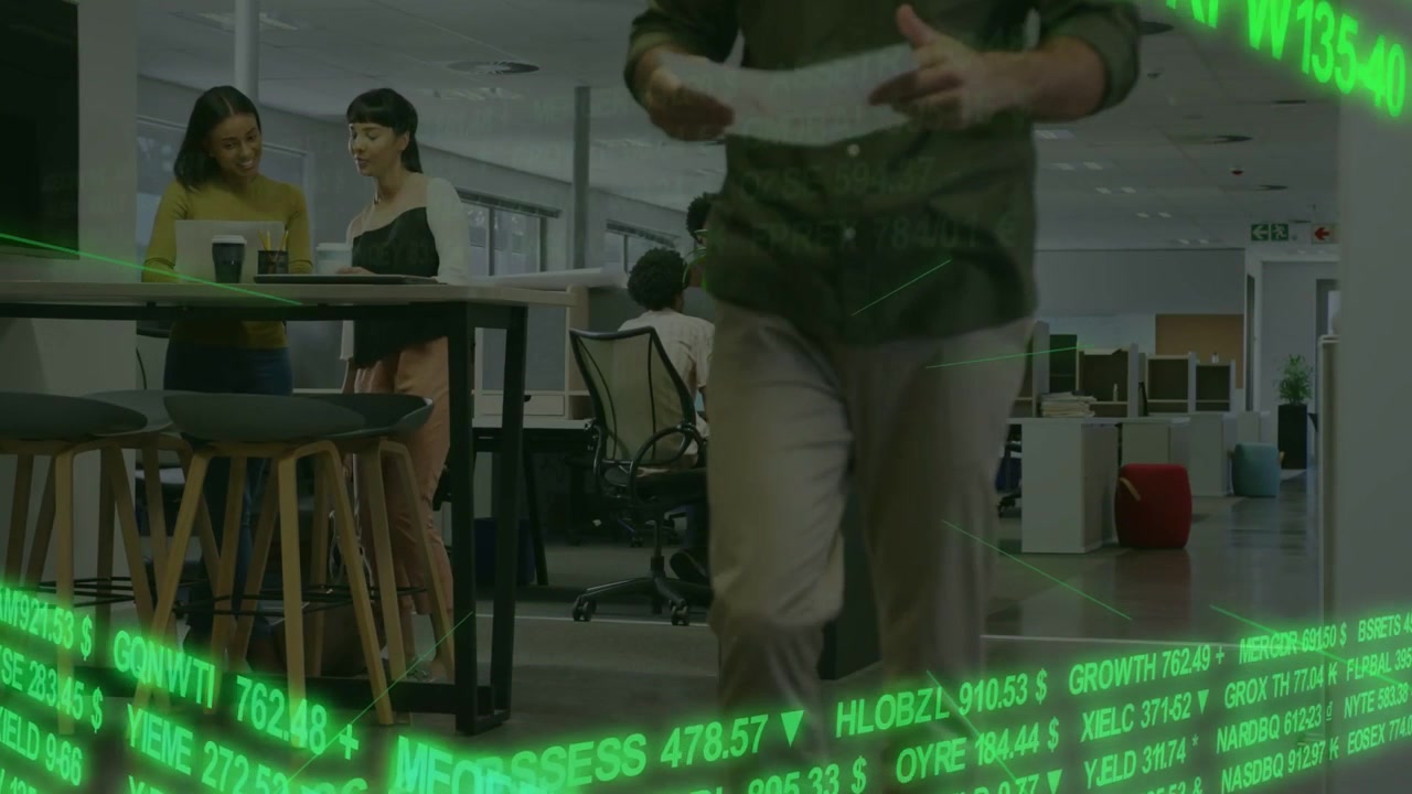 Vertical video: Entering, man in olive shirt smoothing papers walking through office, green ticker