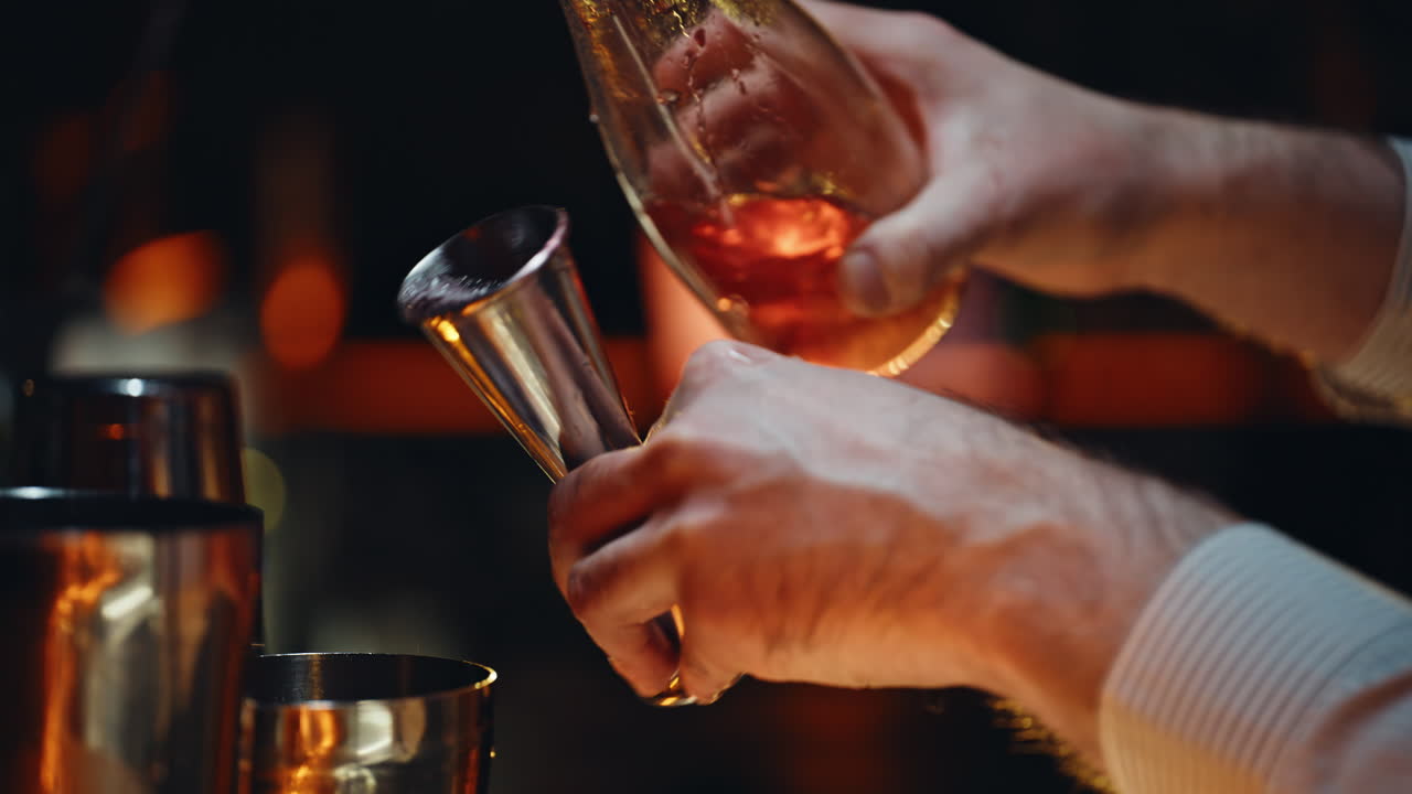 Primo piano di un barista che versa un drink in un misurino mentre prepara un cocktail in un pub