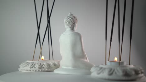 close up shot of a buddha's mini statue placed between rotating incense sticks and candles