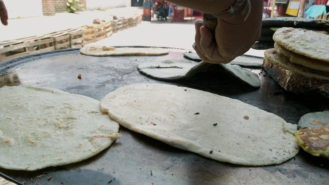 Closeup view of street food vendor preparing fresh quesadillas on hot metal griddle at busy outdoor market during daytime with traditional cooking process and local cuisine