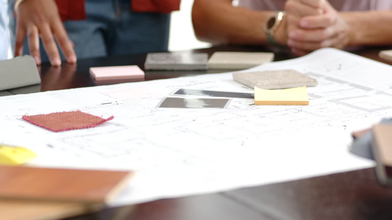 Diverse team pointing at samples at table, selecting swatches and reviewing plan with yellow pencil