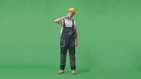 full body of asian man worker wearing goggles and safety helmet showing thumbs down gesture to camera while standing in the green screen background studio