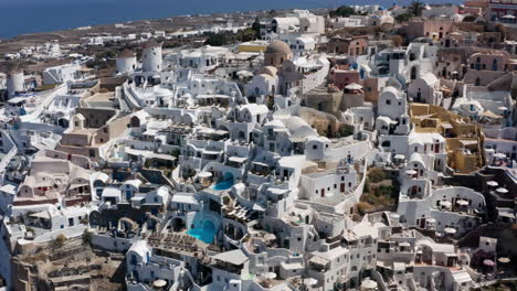 Edificios-Blancos-Tradicionales-En-El-Pueblo-De-Oia-Y-El-Mar,-Isla-De-Santorini,-Grecia---Retroceso-Aéreo