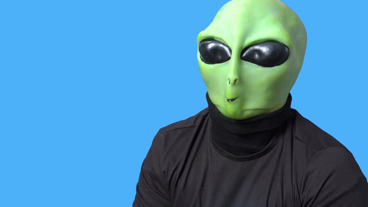 artista profesional en traje alienígena y en una camiseta negra se ríe y agarra su cabeza en histeria contra el fondo azul chromakey. ensayo de papel